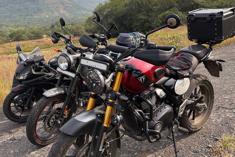 Three motorcycles parked alongside the mountain road leading to Savlya Ghat, with the RE Scram 411, Yamaha R15 V3, and Triumph standing ready against the backdrop of the winding route through the Sahyadri hills.