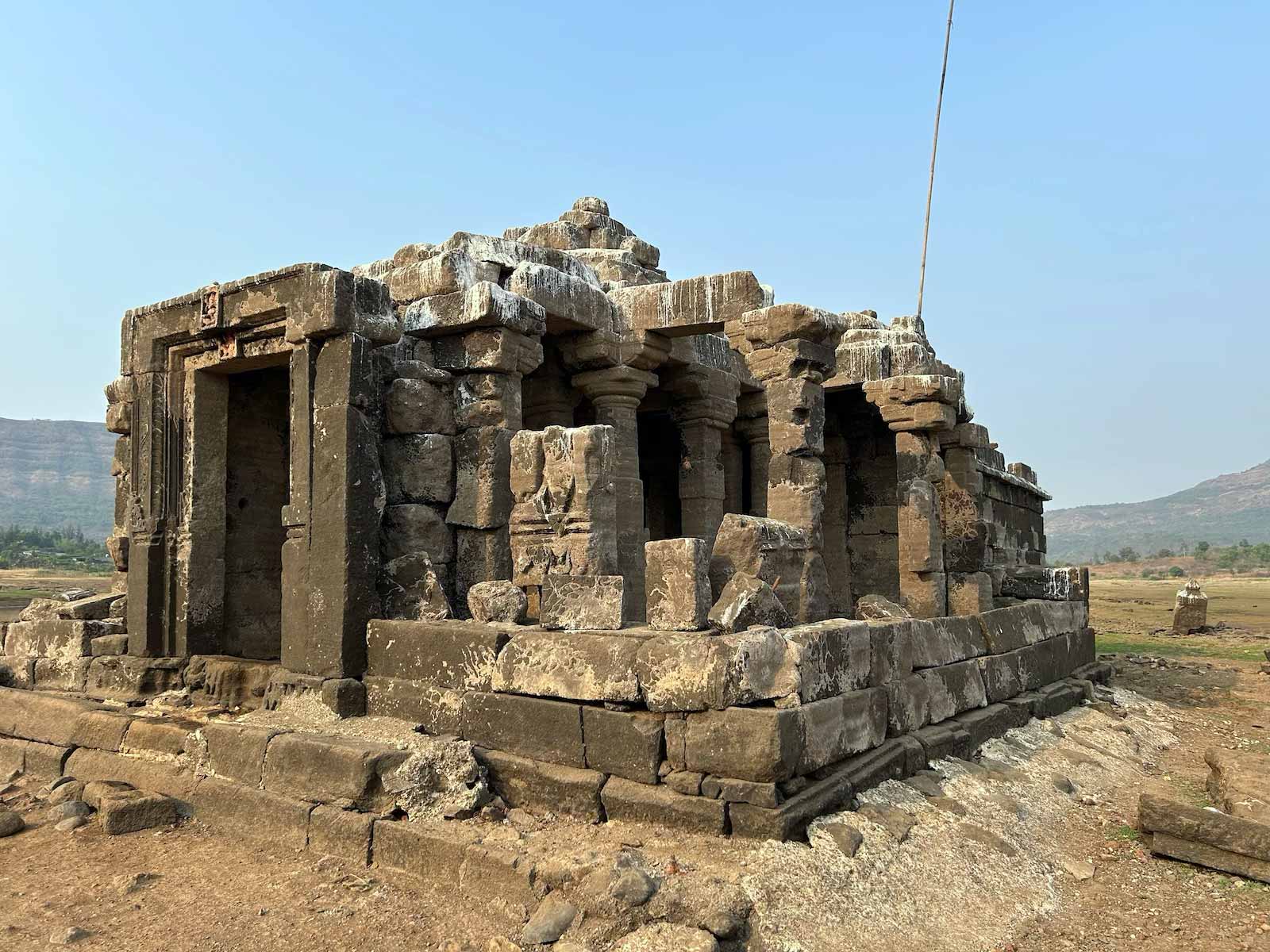 Centuries-old Wagheshwar Temple standing on dried lakebed, showing weathered stone structure with pillars and distinctive architecture from the Chalukya period, normally submerged under Pawana Dam waters