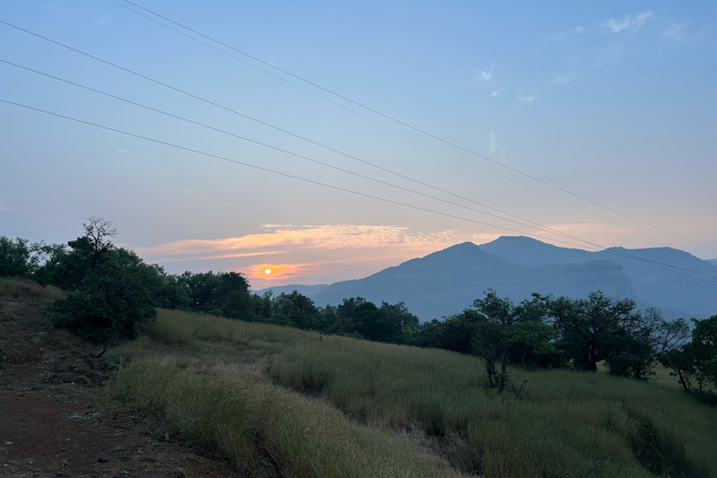 Breathtaking sunrise view from Tamhini Ghat with golden sunlight breaking through the hills, illuminating the lush green vegetation and creating a dramatic silhouette of the undulating Western Ghats landscape