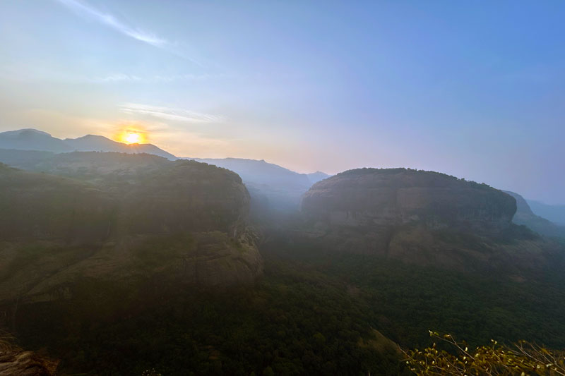 Breathtaking sunrise illuminating the distinctive mushroom-shaped mountain at Savlya Ghat, with golden light spilling across the misty Kundalika Valley below and the dramatic cliff faces of the Sahyadri range in the background