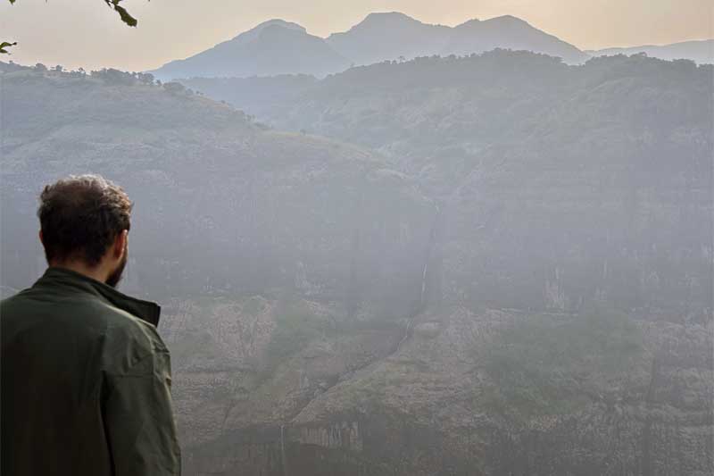 Remarkable view of multiple waterfalls still cascading down the vertical cliff faces of the Sahyadri range two months after monsoon season has ended, creating silvery ribbons against the dark rock as seen from Savlya Ghat plateau.