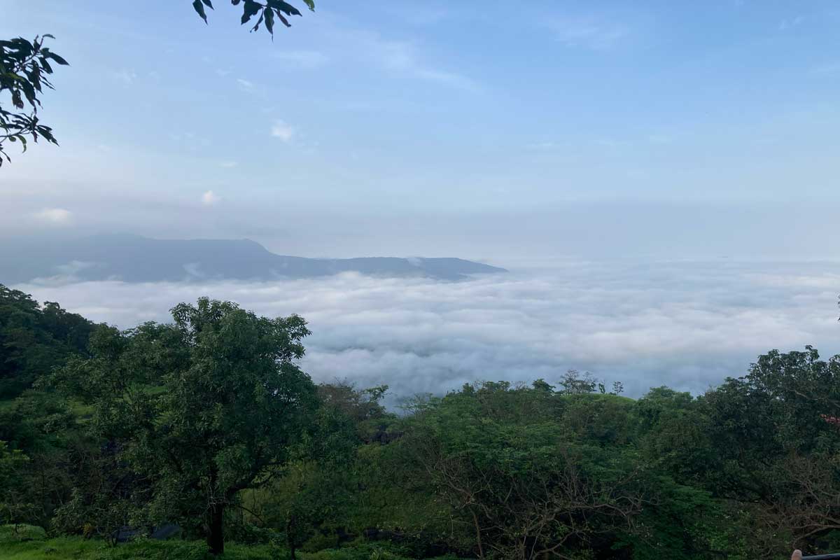 Breathtaking view of a sea of clouds below Tamhini Ghat mountain pass in the early morning, with lush green vegetation framing the misty valley landscape