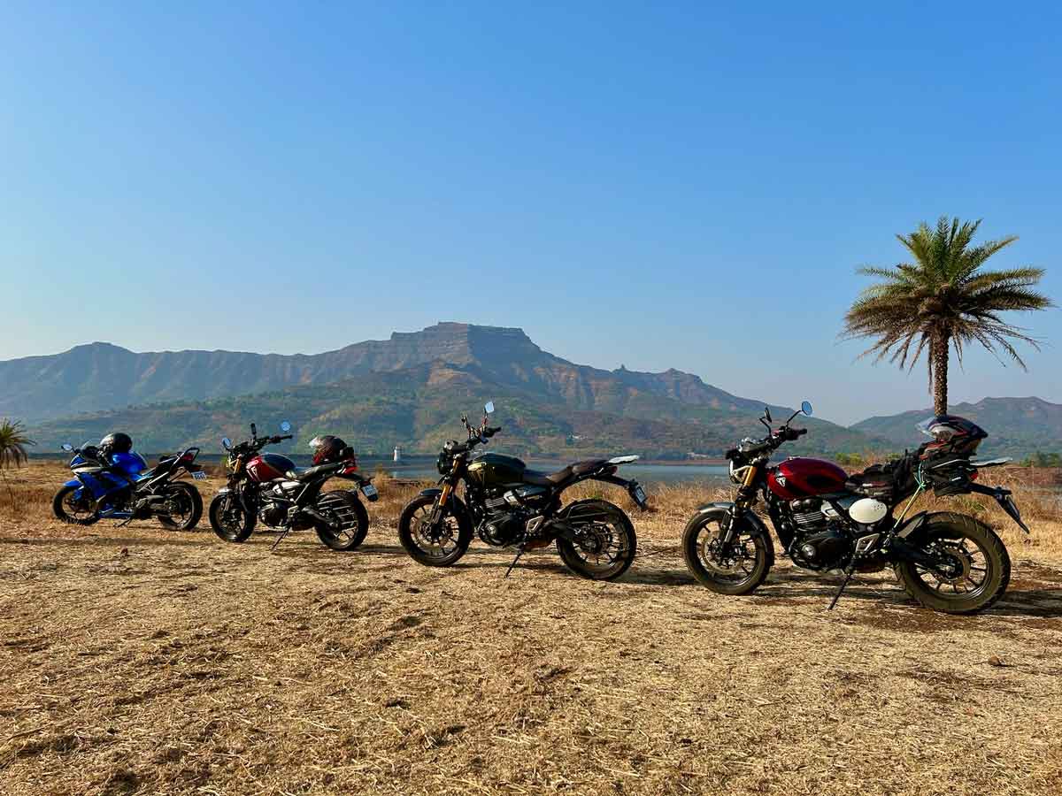 Four motorcycles lined up at Gunjavne Dam with Torna Fort in the background - showing the Kawasaki Ninja and three Triumph motorcycles used for the Kadve Ghat expedition