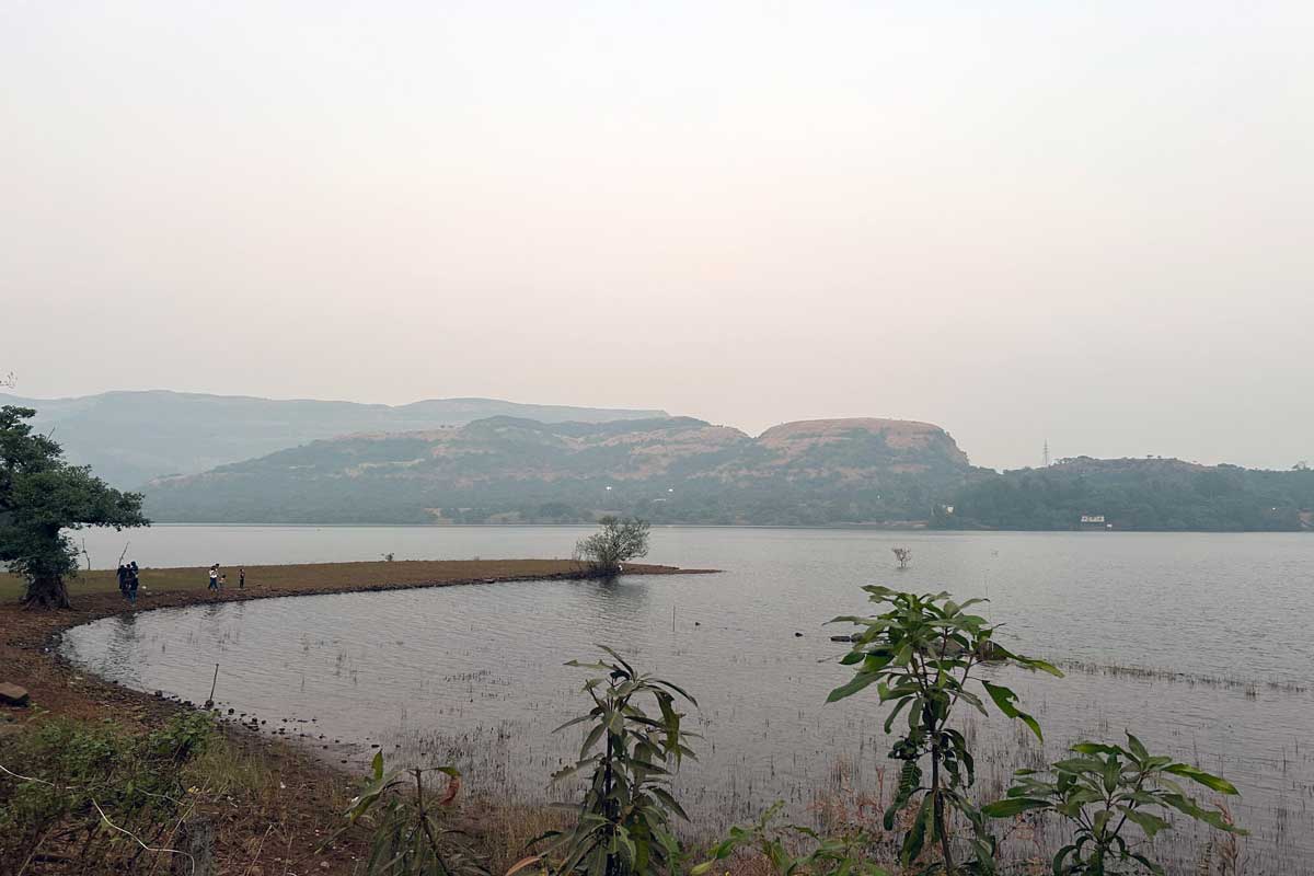 Calm reflective waters of Mulshi Dam backwaters surrounded by lush green hills of the Western Ghats, with morning light illuminating the verdant ghat section landscape